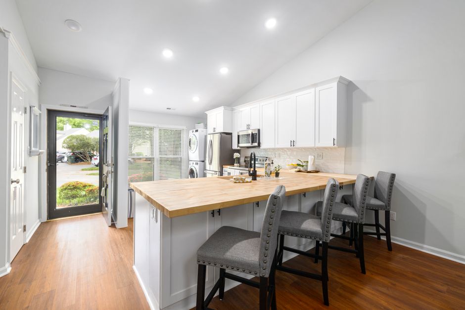 A bright modern kitchen with a wooden countertop, white cabinets, and bar stools.